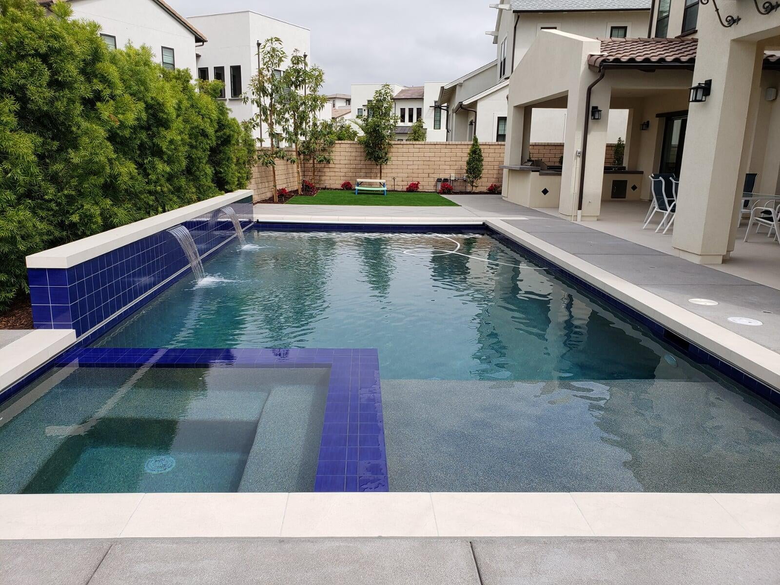 Modern rectangular pool with sheet-descent water wall and attached outdoor kitchen, built by UltraScape in San Diego County